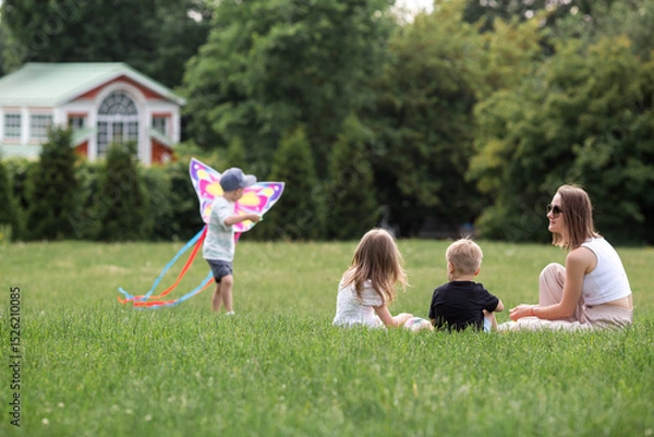 Fototapeta A family with three children. A mother with many children and toddlers in a summer park. Children are walking and flying a kite. Large families, family values, and leisure time with children.