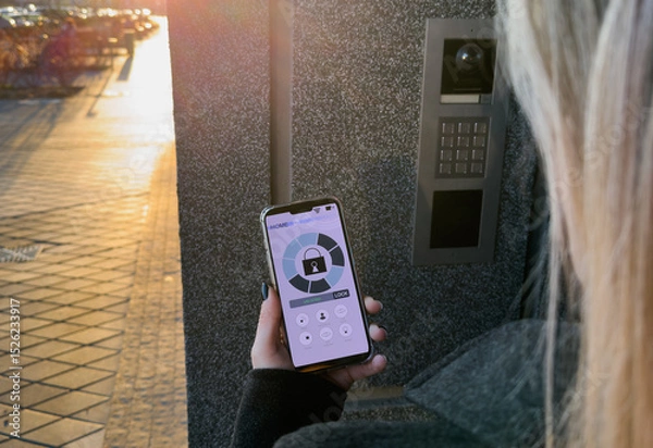 Fototapeta A Person's Hand Holding Smartphone For Disarming Security System Of Door