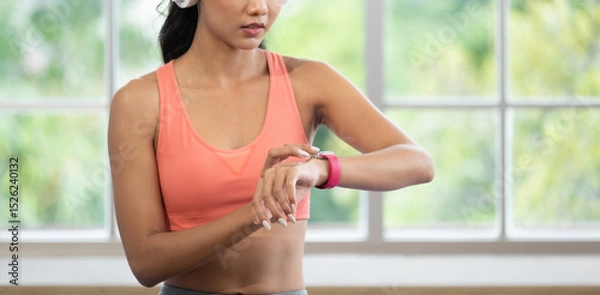 Fototapeta young healthy asian woman use smart watch to measure heart rate after exercise at home