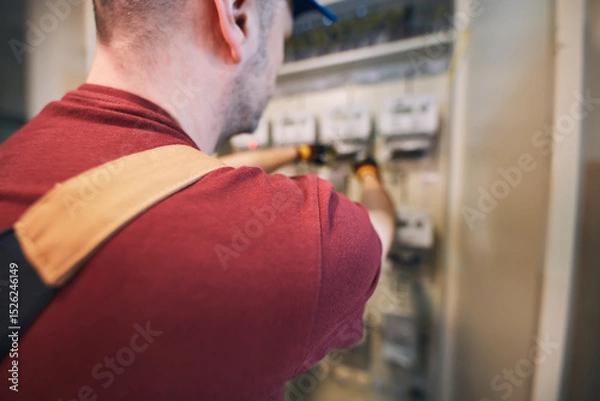 Fototapeta Electrician working on a modern electricity power meter station in a building.