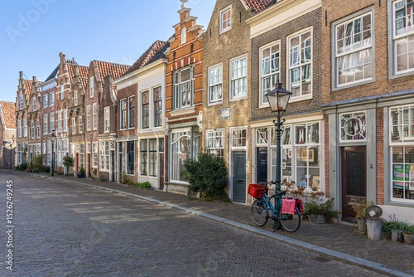 Obraz Capturing the timeless charm of a Dutch street in Dordrecht, this image showcases a row of classic gabled houses with facades and a lone bicycle. Dordrecht, Netherlands. 16 March 2025.