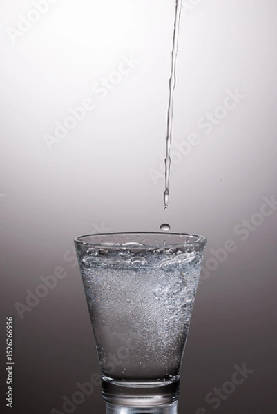 Fototapeta A crystal-clear stream of water pours gracefully into a glass, captured in mid-motion with sharp detail and precision.