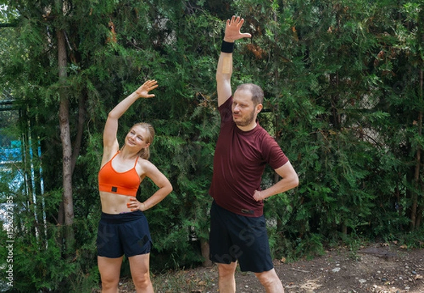 Obraz Active young couple stretching outdoors before a workout. Man and woman doing warm-up exercises in a park. Healthy lifestyle concept.
