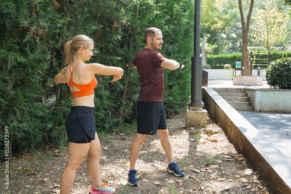 Obraz Active couple warming up before a workout.  They perform stretching exercises in a park. Healthy lifestyle concept.