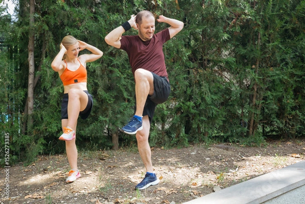 Obraz Man and woman doing high knee exercises outdoors.  Active couple working out together in a park, improving fitness and health.  Great for fitness, wellness, and healthy lifestyle concepts.