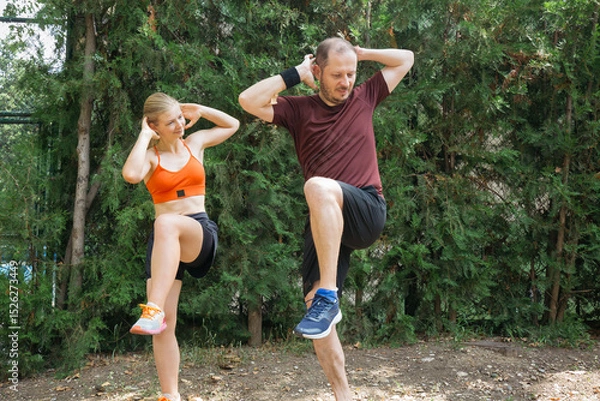 Obraz Active young couple doing high knee exercises outdoors.  Man and woman in sportswear exercising together in a park. Healthy lifestyle concept.
