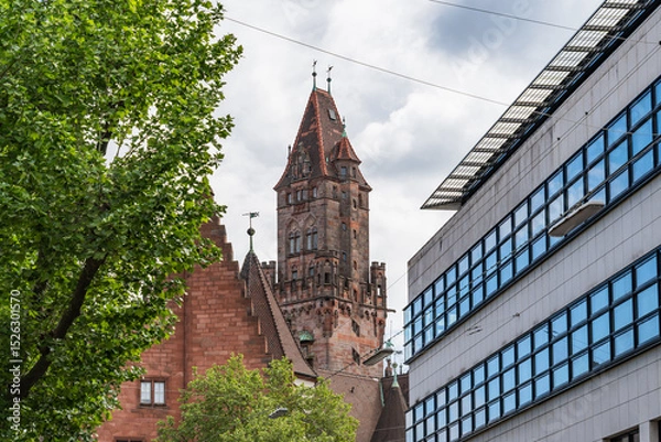 Fototapeta A tall building with a clock tower and a tree in front of it in Saarbrucken Germany