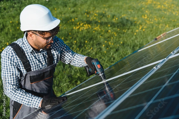 Fototapeta Technician installing solar panel in green field using screwdriver