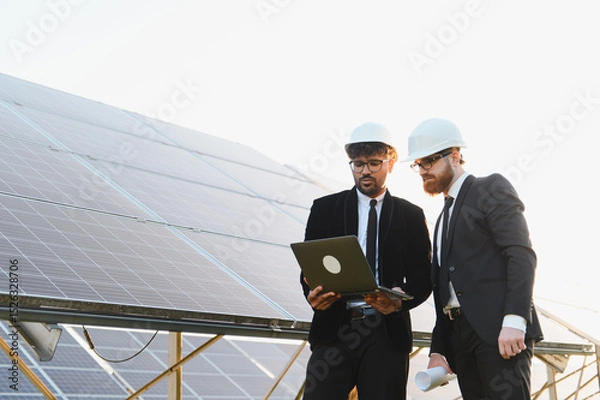 Fototapeta Engineers using laptop analyzing solar panel farm for renewable energy