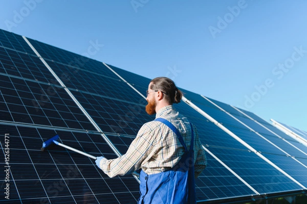 Fototapeta Technician cleaning solar panels in a solar farm for green energy production
