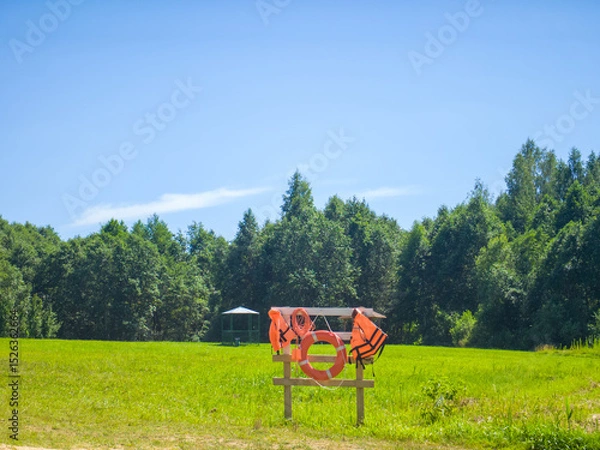 Obraz A lifebuoy and life jacket are hanging on a wooden fence the backdrop of a forest.