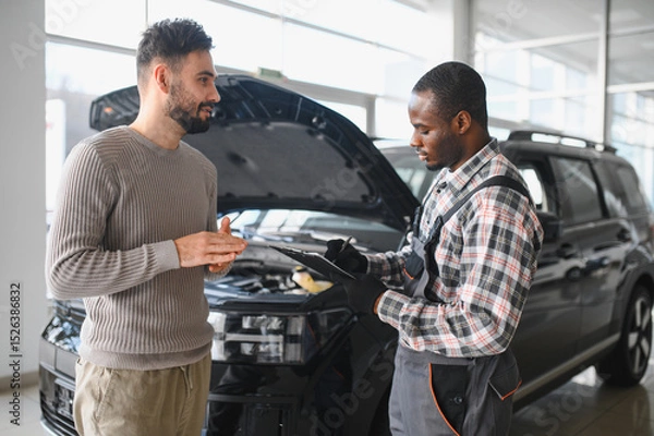 Fototapeta Mechanic, car servicing at garage - concept of timely customer service, car maintenance and deal agreemnet