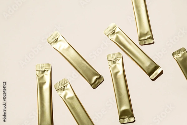 Fototapeta Several Golden Stick Packaging Sachets on Light Background. Unbranded Foil Pouch Mockup for Product Presentation.