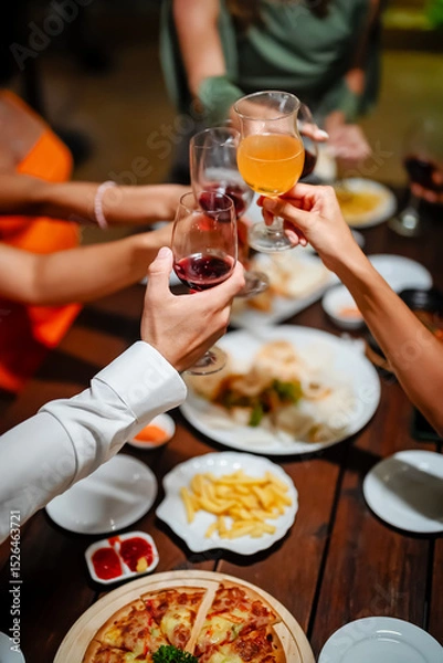Fototapeta Close-up of friends sharing a delicious meal and drinks at a lively dinner party, featuring seafood, fries, and wine on a wooden table