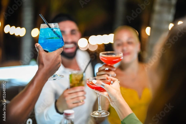 Fototapeta A group of young adults socializing at a lively outdoor bar at night, enjoying colorful cocktails and engaging in cheerful conversation.