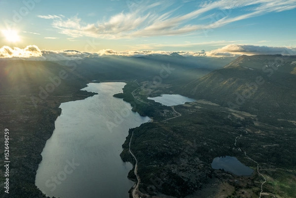 Fototapeta Sun rays pierce clouds over lake and smaller bodies of water surrounded by forested mountains in Patagonia under a partly cloudy sky