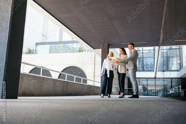 Fototapeta Business team reviewing contract terms on digital tablet in modern office building. View from below.