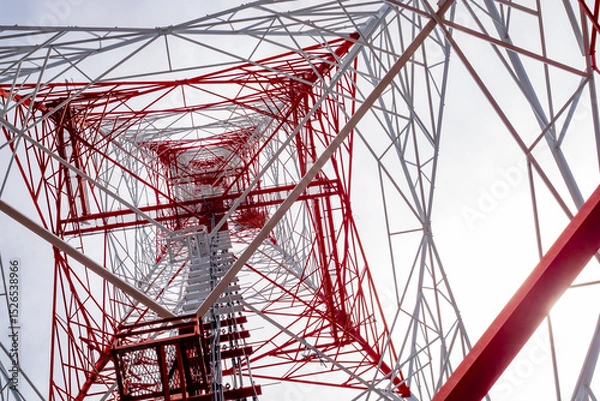 Fototapeta Low-angle view of a red and white telecommunications tower structure against a bright sky, highlighting modern engineering, symmetry, and industrial design.
