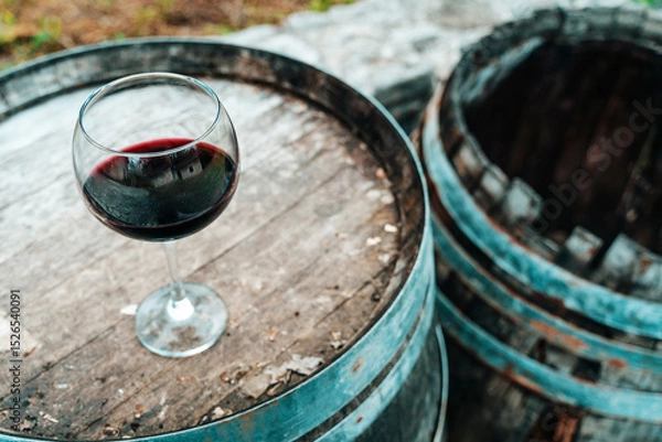 Fototapeta Glass of Red Wine on Old Oak Barrel in Rustic Cellar