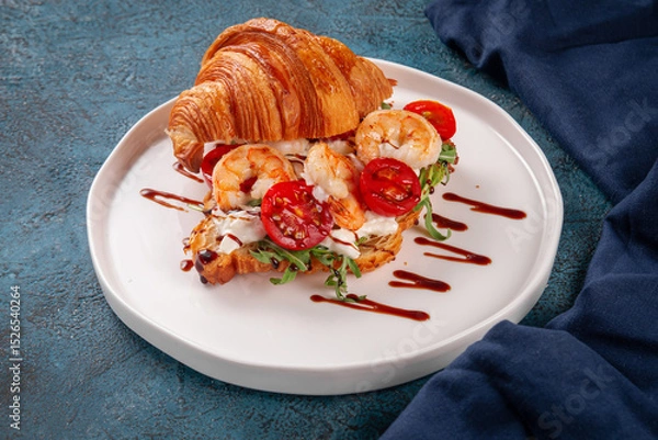 Fototapeta Delicious croissant sandwich filled with grilled shrimp, fresh arugula, cherry tomatoes and cream cheese. Topped with balsamic glaze and served on a white plate