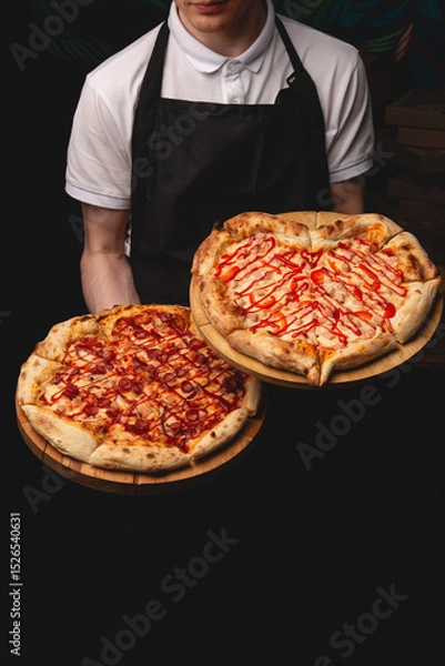 Fototapeta A server in a white polo and black apron presents two freshly baked pizzas. One is a classic pepperoni with a crispy golden crust and vibrant red sauce drizzle. The other shaped like a heart