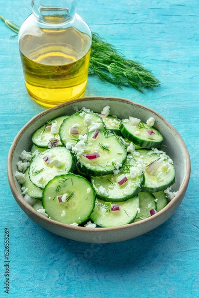 Fototapeta Cucumber salad with dill, red onion, and Feta cheese, on a blue background, with ingredients