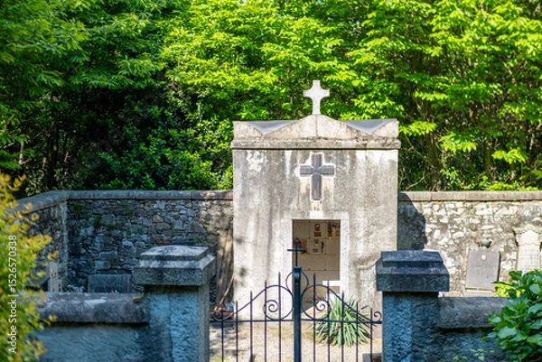 Obraz old stone crypt with prominent cross, surrounded by lush green foliage, ancient traditional religious heritage, Historic Burial Site