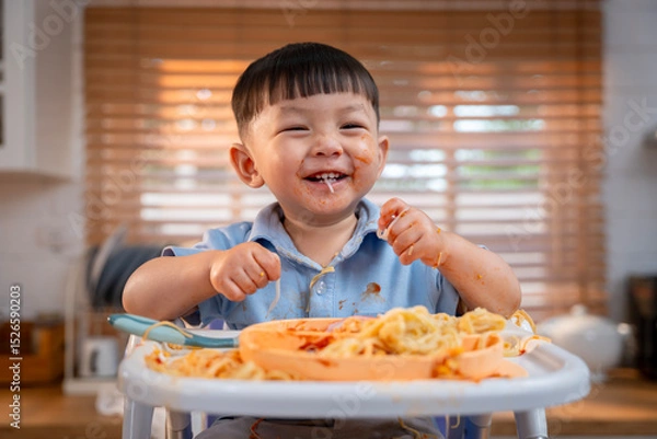 Obraz Happy Asian boy with a big smile, messy face, enjoying a fun mealtime.
