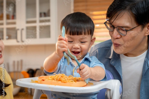 Obraz Boy happily eats spaghetti with parents in a warm family setting.