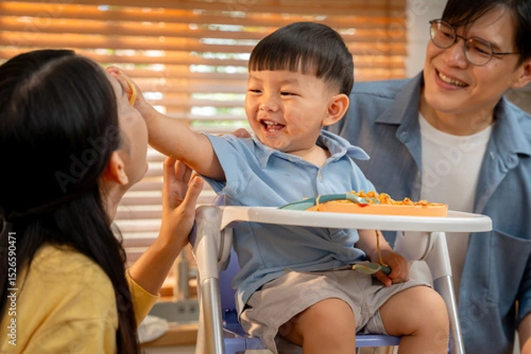 Obraz Happy family moment. A smiling boy enjoys mealtime with parents.
