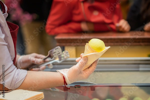 Fototapeta Close-up of vendor holding yellow ice cream cone over counter in public place. Concept of ice cream, frozen product in summer, sweet craving, refreshment. Small business support