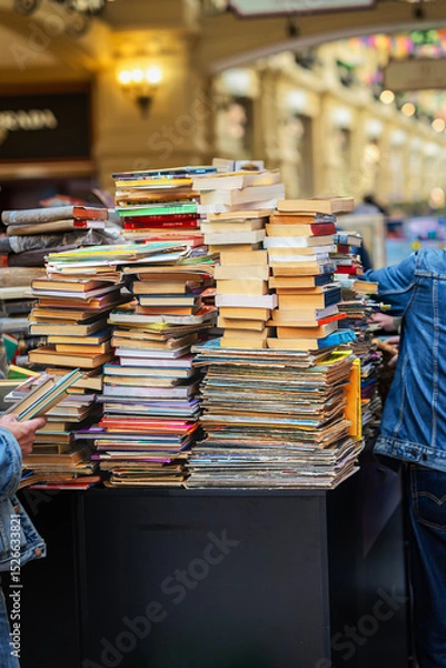 Fototapeta Stacked used books, sale on market. Messy stacks of old and new books on market table with people browsing. Concept of books, used literature, vintage finds and casual book market