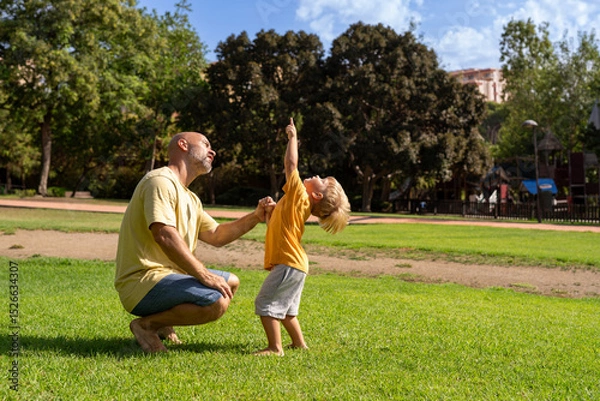 Fototapeta Cheerful father and son looking at each other while laughing at park on sunny day. father and son hugging in the park. communication between father and little son