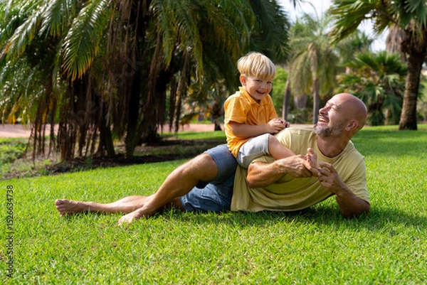 Fototapeta cheerful father plays with his son in the park. father and son on the green lawn having fun