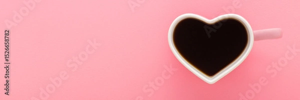 Fototapeta Heart shape white cup with fresh black coffee on light pink table background. Pastel color. Wide banner. Closeup. Empty place for text. Top down view.