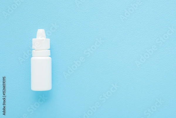 Fototapeta New white plastic bottle of medical liquid for eyes, nose or ears on light blue table background. Pastel color. Closeup. Empty place for text. Top down view.
