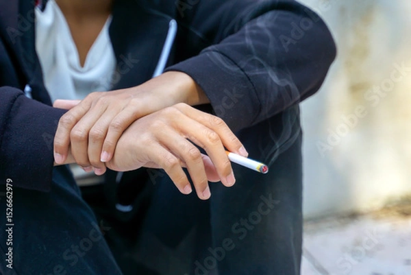 Fototapeta young man uses his hand to pick up a cigarette while sitting alone smoking. Soft and selective focus.