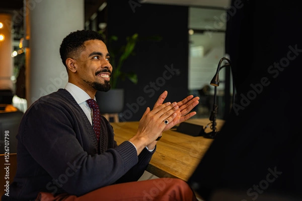 Fototapeta Young businessman sitting at a wooden table and clapping hands during a meeting in a modern office