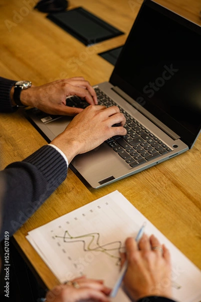 Fototapeta Business colleagues working together, analyzing financial data on charts and using laptop, during a productive office workday