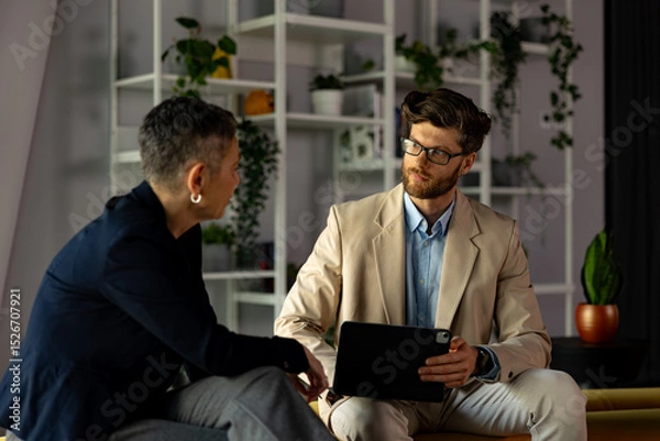 Fototapeta Businessman presenting a project on a tablet while engaging in discussion with a businesswoman in a modern office setting