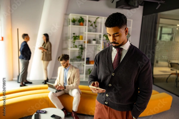 Fototapeta Businessman using smartphone in modern office with colleagues working in background, concept of technology and business