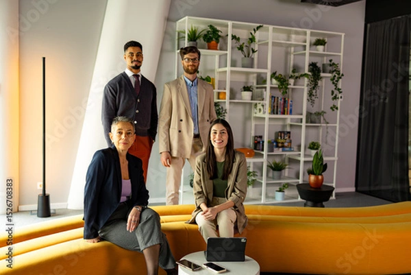 Fototapeta Four businesspeople posing confidently in a modern office, surrounded by greenery and featuring a stylish yellow sofa, embodying teamwork