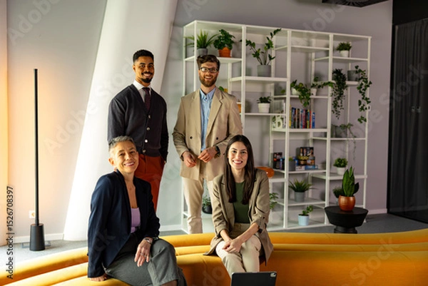 Fototapeta Four startup businesspeople posing together in a bright, modern office, surrounded by greenery and a stylish white bookshelf