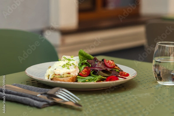 Obraz Delicious Eggs Benedict served with a side salad on a rustic plate for a perfect outdoor brunch on a summer day.Close-up of a gourmet brunch plate. Poached eggs on toast with fresh salad and cutlery