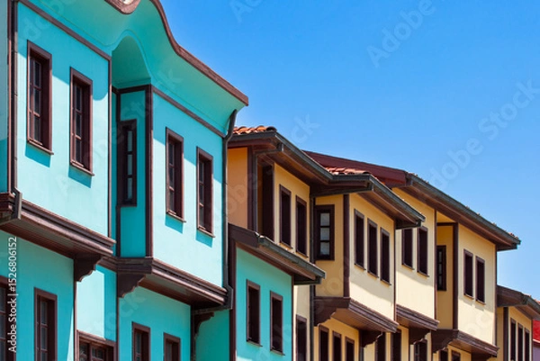 Fototapeta 
Traditional Ottoman-era houses with distinctive turquoise and yellow facades line a street in Odunpazari, Eskisehir, under a clear blue sky. The vibrant architecture reflects the rich historical char