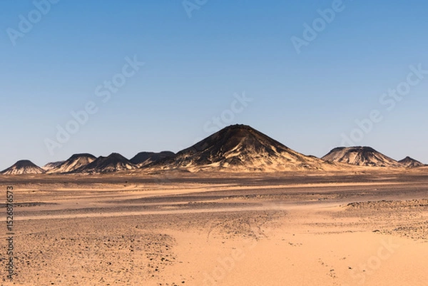 Fototapeta Ash-covered hills in Egypt's Black Desert under a clear sky, scenic and remote landscape. Volcanic