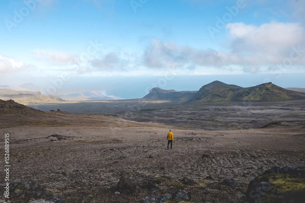 Fototapeta Lone traveler in a yellow jacket walks across Iceland’s volcanic highlands toward the distant coastline, surrounded by raw beauty and the vastness of Snafellsnes Peninsula