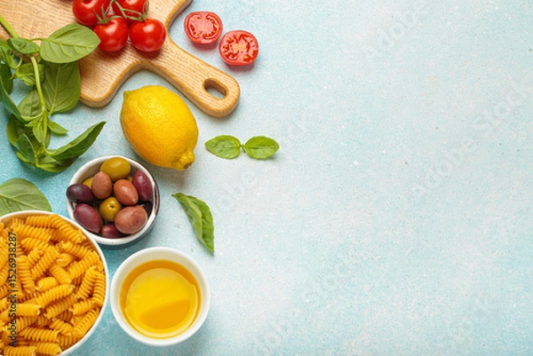 Obraz Cherry tomatoes, basil, olives, lemon, olive oil, fusilli pasta and wooden cutting board are creating a frame with copy space on a light blue background, concept of Italian cuisine cooking, copy space