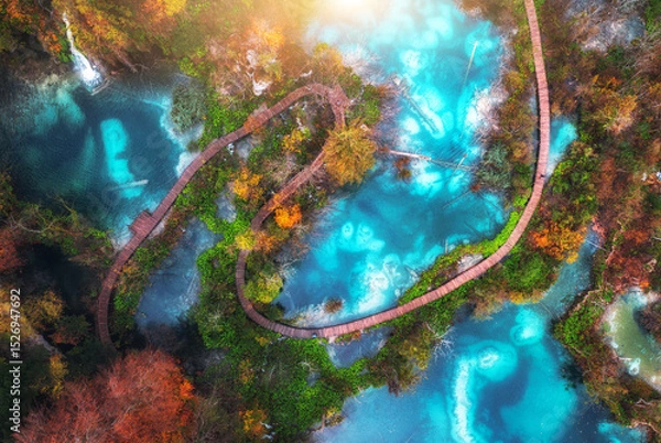 Obraz Aerial view of blue lakes in red autumn forest at sunrise. Morning in Plitvice Lakes park, Croatia. Colorful landscape with azure water, trees, wooden trails and bridges, orange foliage. Top view