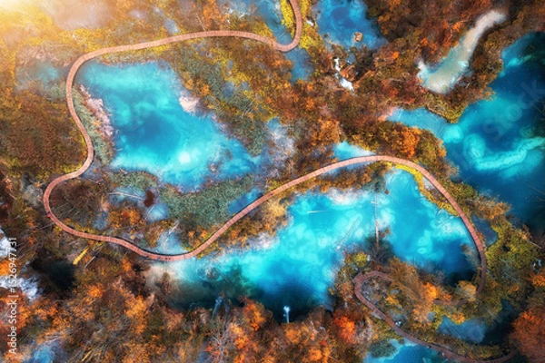 Obraz Aerial view of blue lakes in red autumn forest at sunrise. Morning in Plitvice Lakes park, Croatia. Colorful landscape with azure water, trees, wooden trails and bridges, orange foliage. Top view